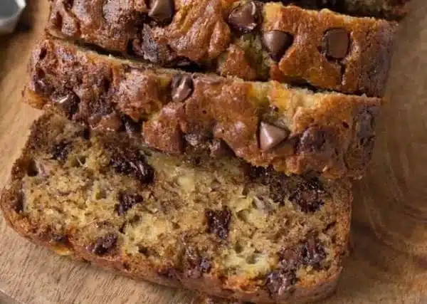 Sliced chocolate chip banana bread on a wooden board with chocolate chips