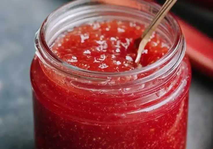 Homemade rhubarb sauce in a glass jar with fresh rhubarb stalks
