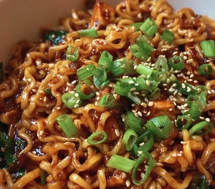 Bowl of easy saucy ramen noodles garnished with green onions and sesame seeds.